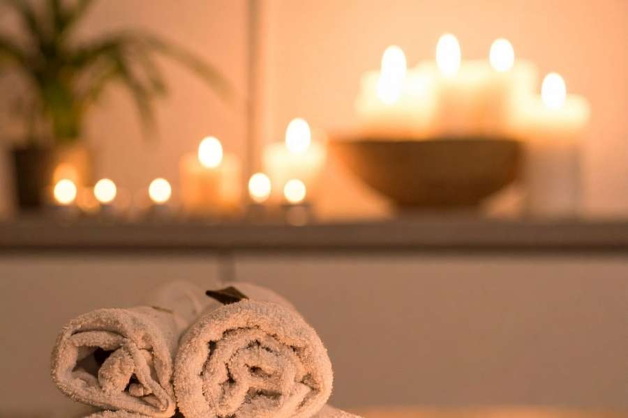 Vue rapprochée de deux serviettes de bain blanches roulées sur une étagère de spa, avec des bougies allumées en arrière-plan.