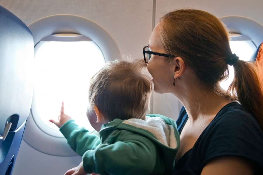 Une maman et son bébé regardent par le hublot en plein vol, illustrant le voyage en avion avec un bébé.